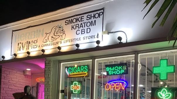 Herbin Living Miami storefront at night with neon signs for CBD, Kratom, and Smoke Shop.