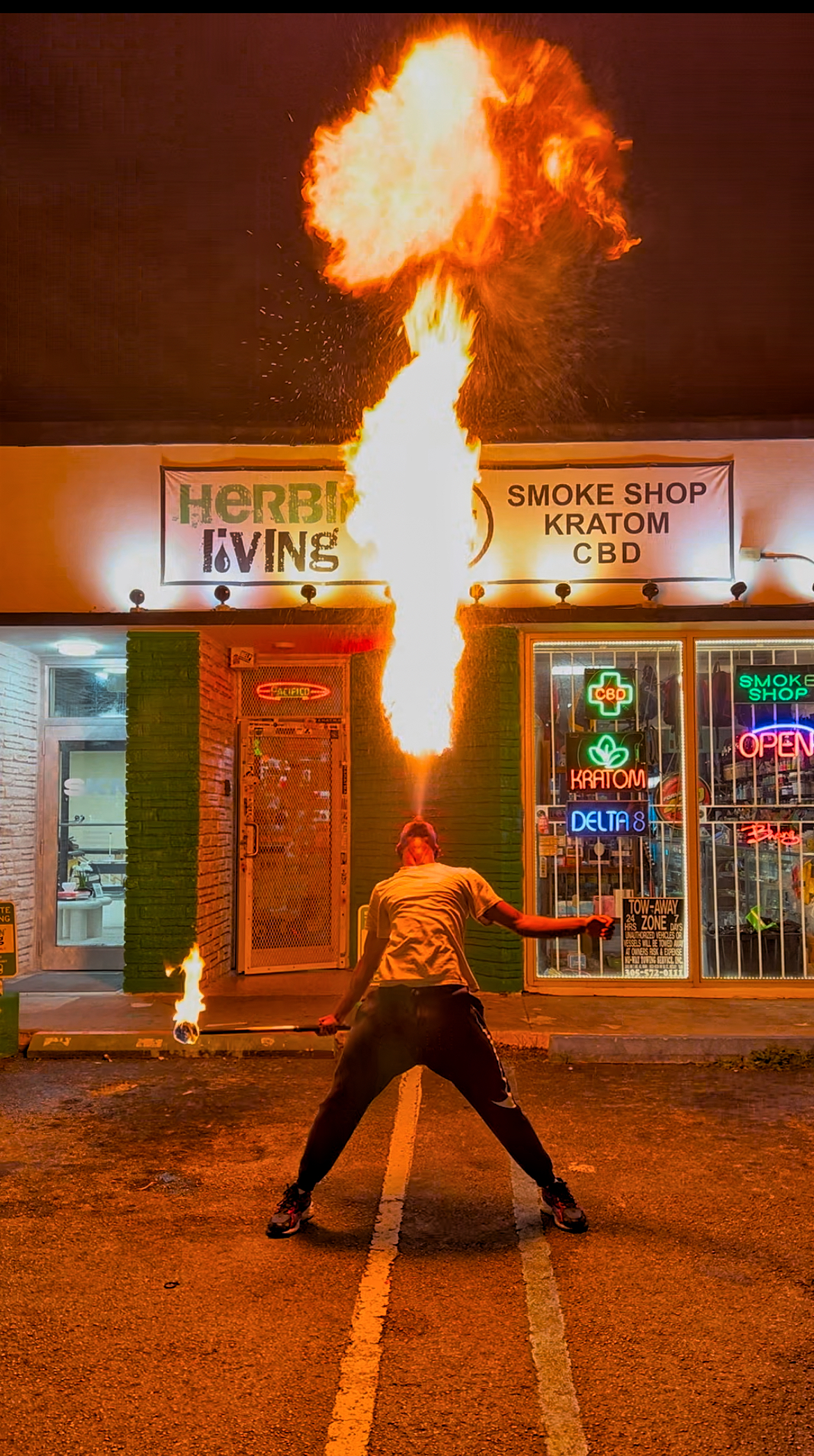 A fire performer breathing fire upward in front of the entrance at Herbin Living